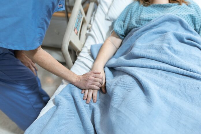 Pielęgniarz trzyma za rękę pacjenta leżącego w łóżku